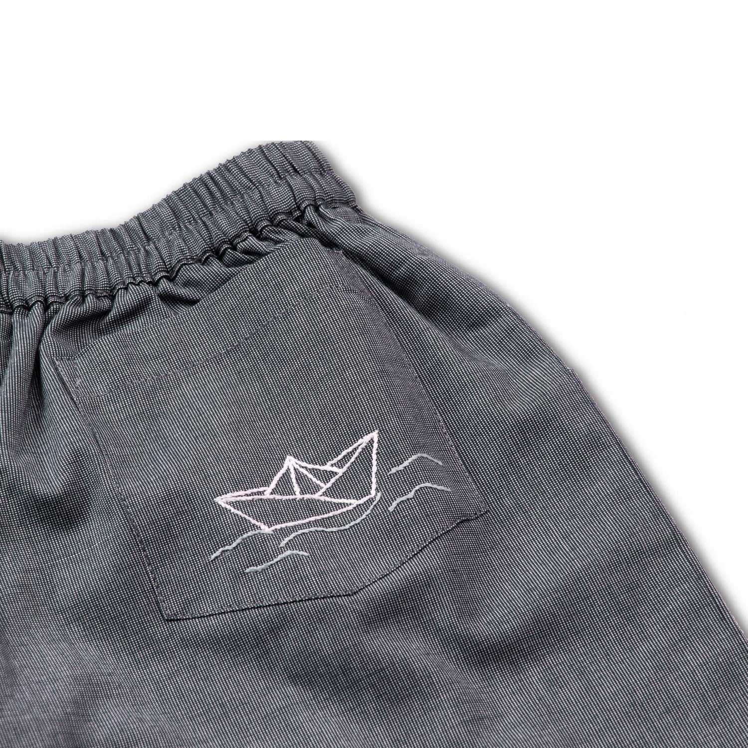 Close up of grey shorts with side and back pockets with hand embroidered paper boats on back pocket