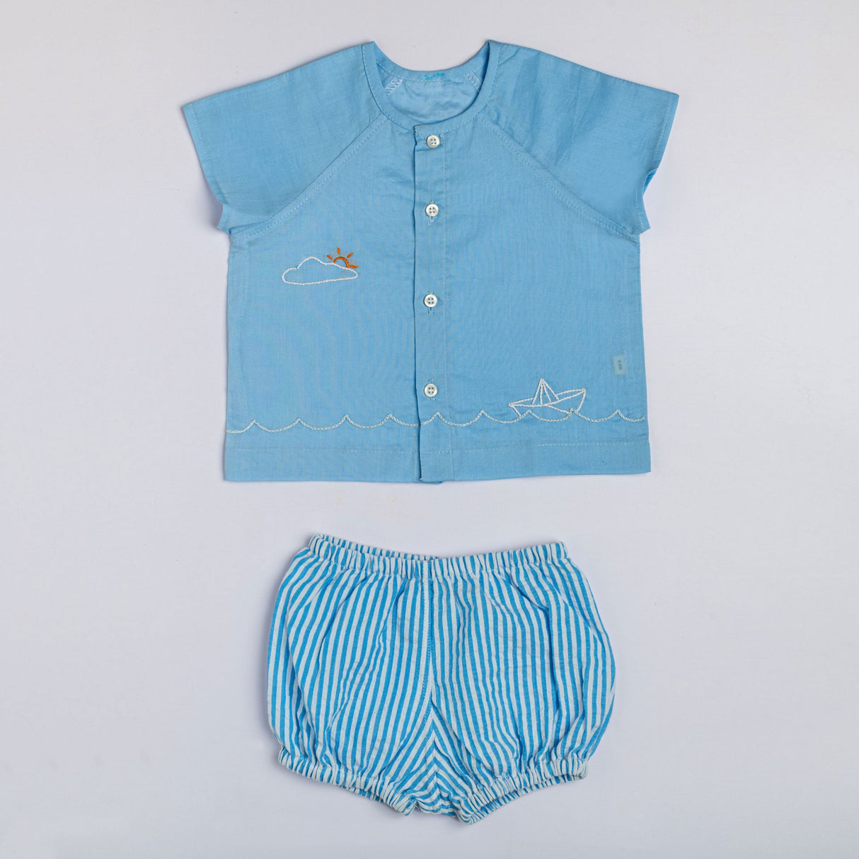 Flatlay of a hand embroidered blue raglan sleeve jabla with a matching striped blue bloomers