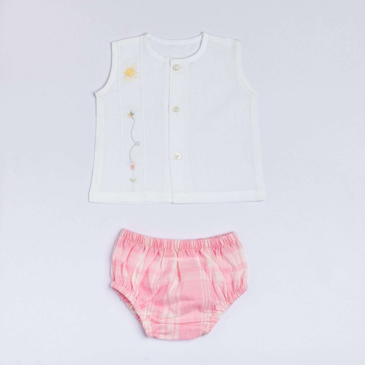 Flatlay of white muslin jabla with front buttons and hand embroidered design paired with pink checked bloomers