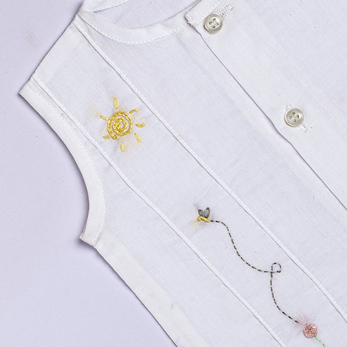 Close up of white jabla with hand embroidered flower and bee with pink plaid bloomers