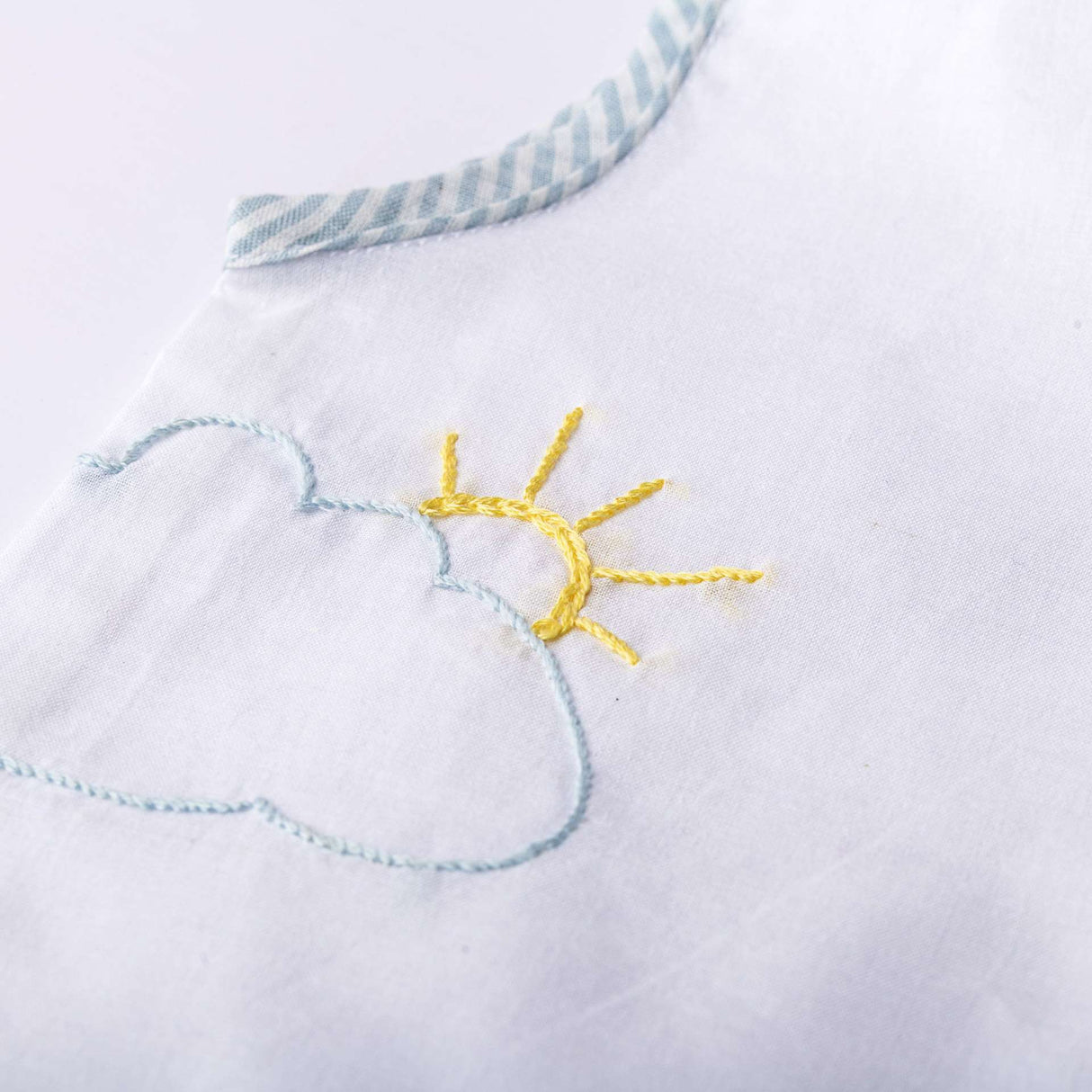 Close up of white jabla with powder blue stripe piping and hand embroidered clouds and sun paired with matching bloomers