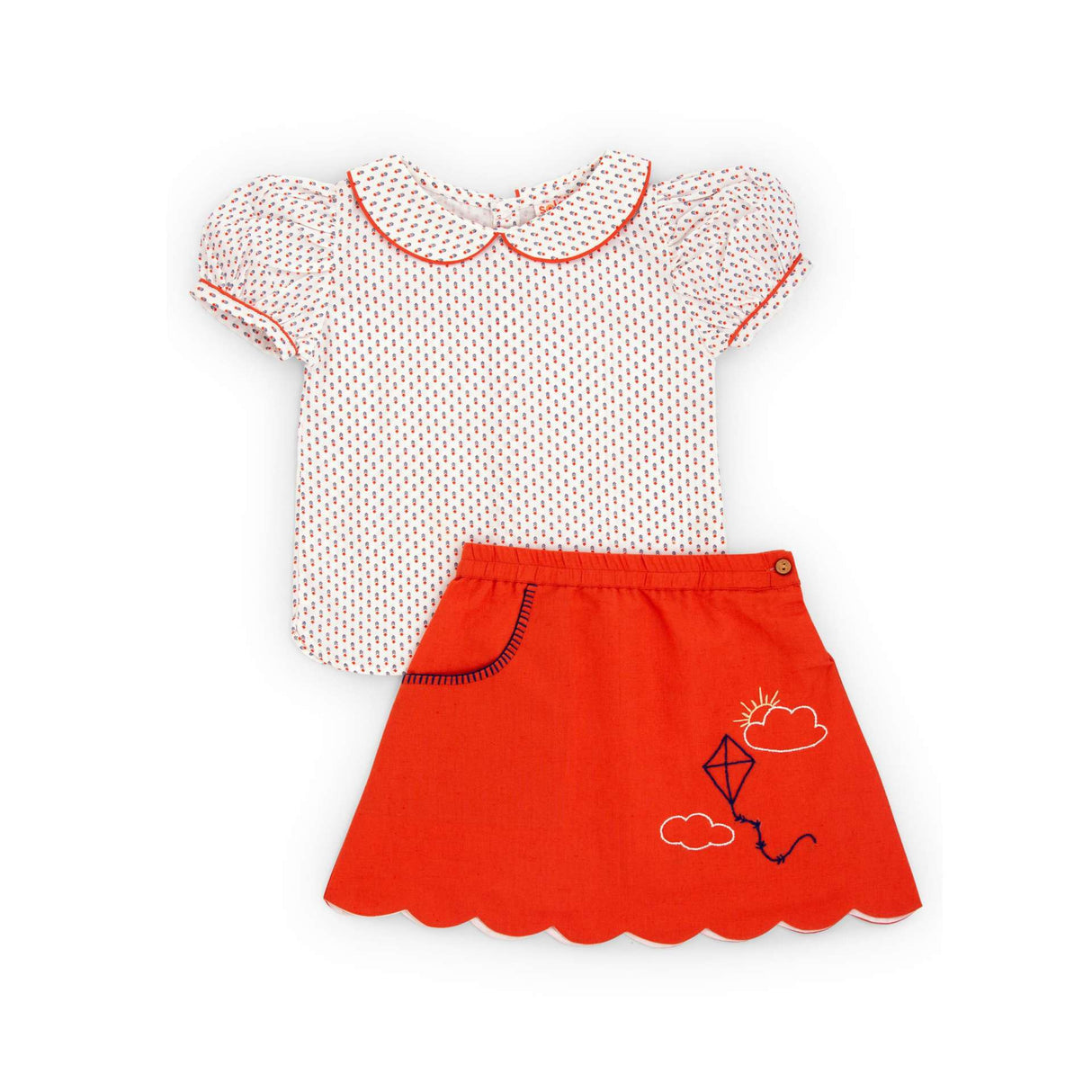 Flat lay of printed blouse matched with a hand embroidered solid orange skirt with a scalloped hem