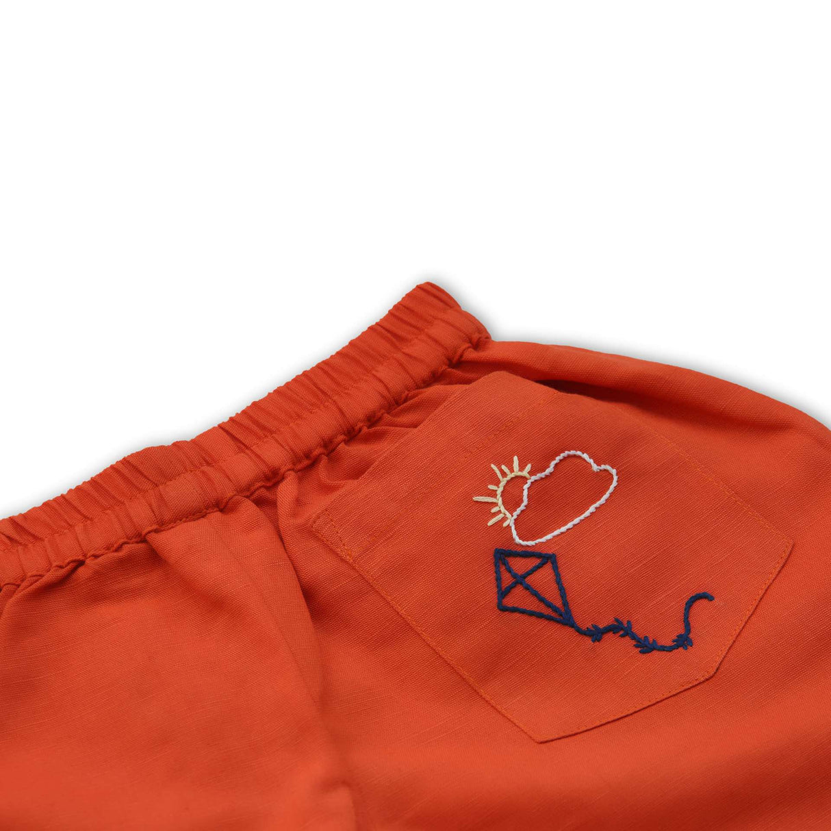 Close up of hand embroidered kite on rear pocket of orange shorts with elastic waistband