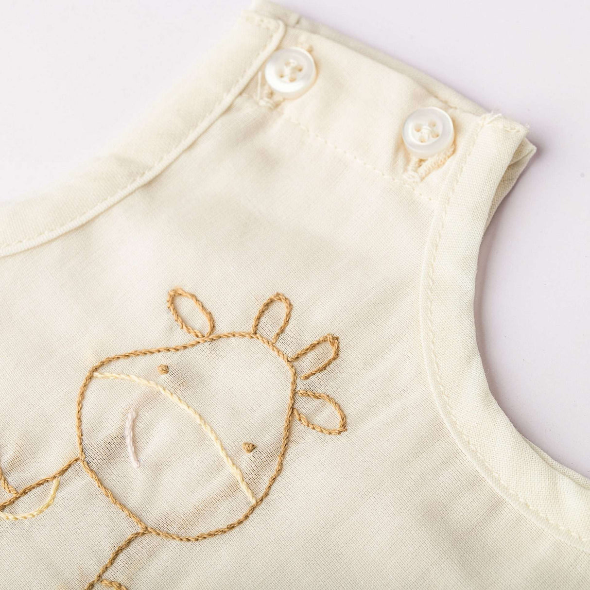 A hand embroidered giraffe and 2 shoulder buttons are visible on a tan infant vest