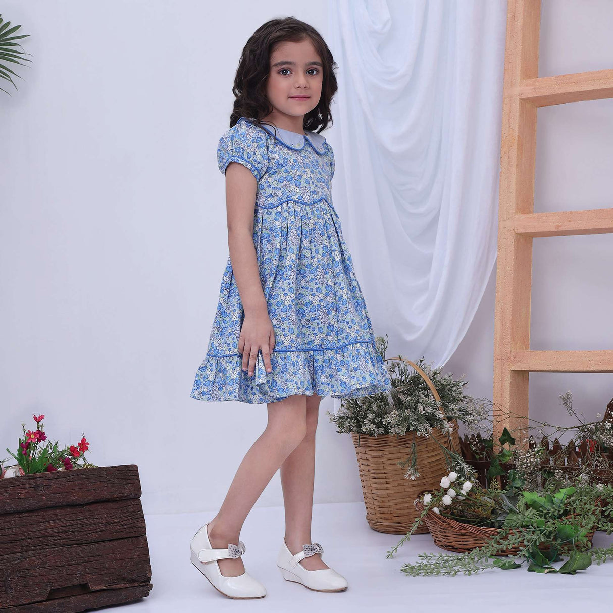 Girl wearing a blue print floral dress with back ties and a hem ruffle
