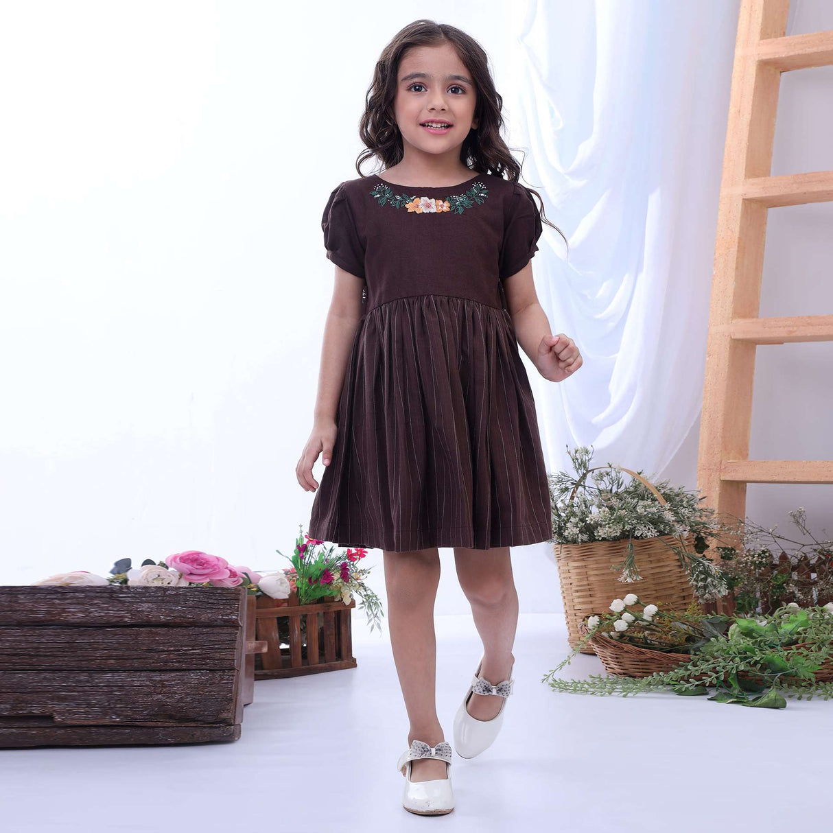 A little girl in a brown chambray dress with a delicate hand embroidered floral neckline