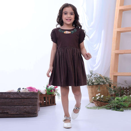 A little girl in a brown chambray dress with a delicate hand embroidered floral neckline