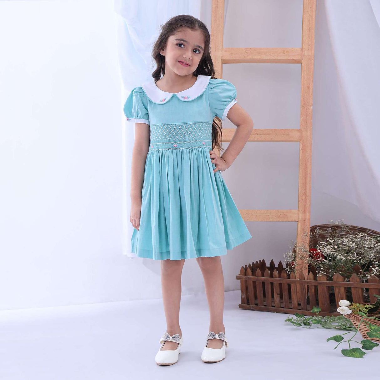 A little girl in turqouise hand smocked dress with hand embroidered collar and cuffs and teal piping