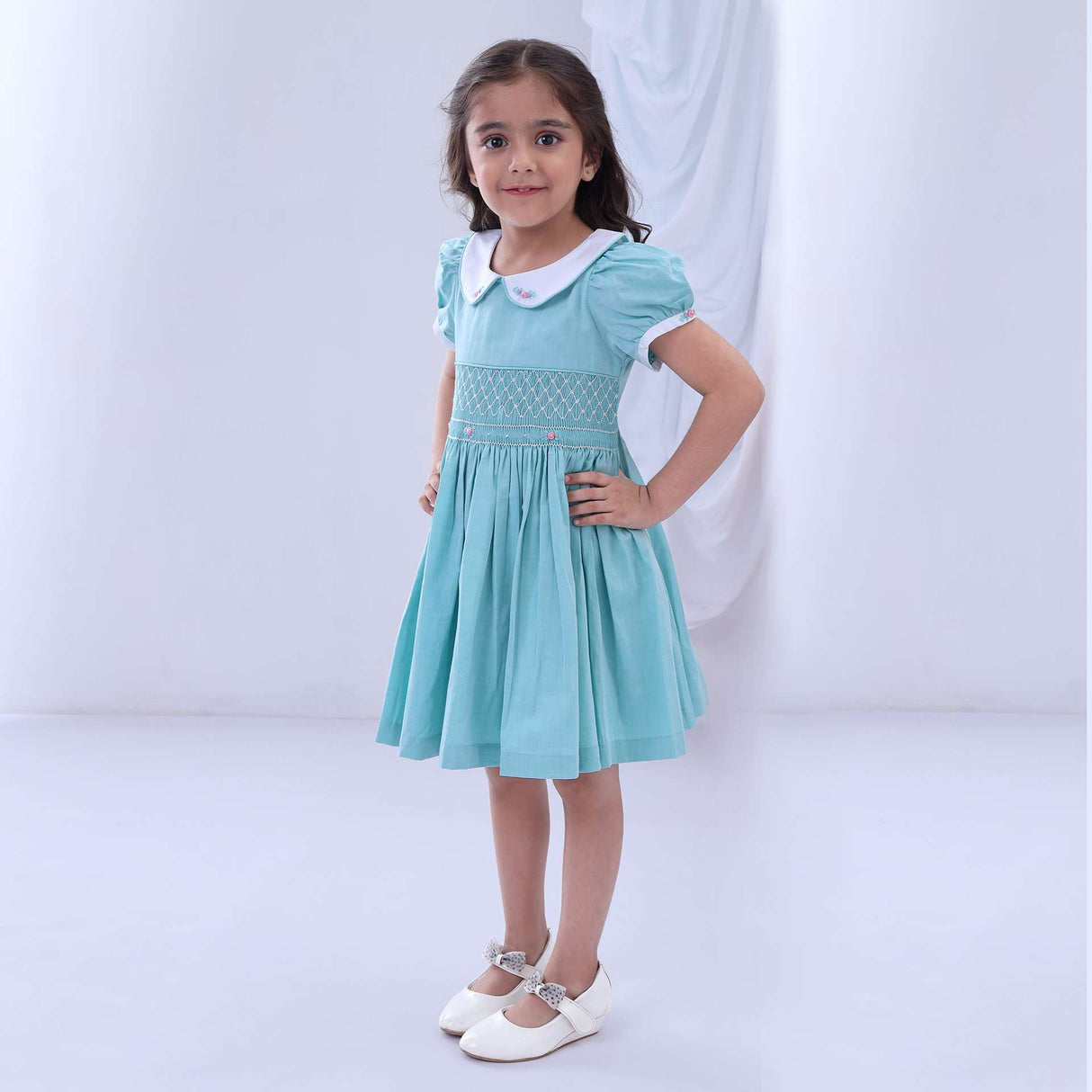 Girl poses in a turquoise chambray hand smocked dress with a white embroidered collar and cuffs