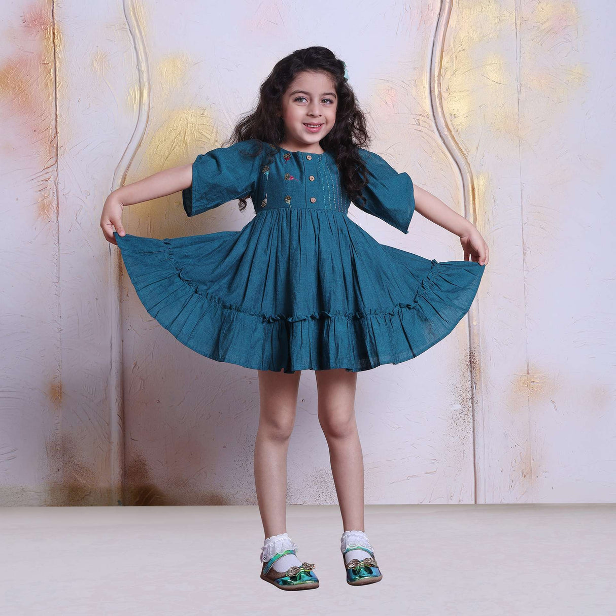 Girl holds up a dress with a wide hem and pretty bodice hand embroidery