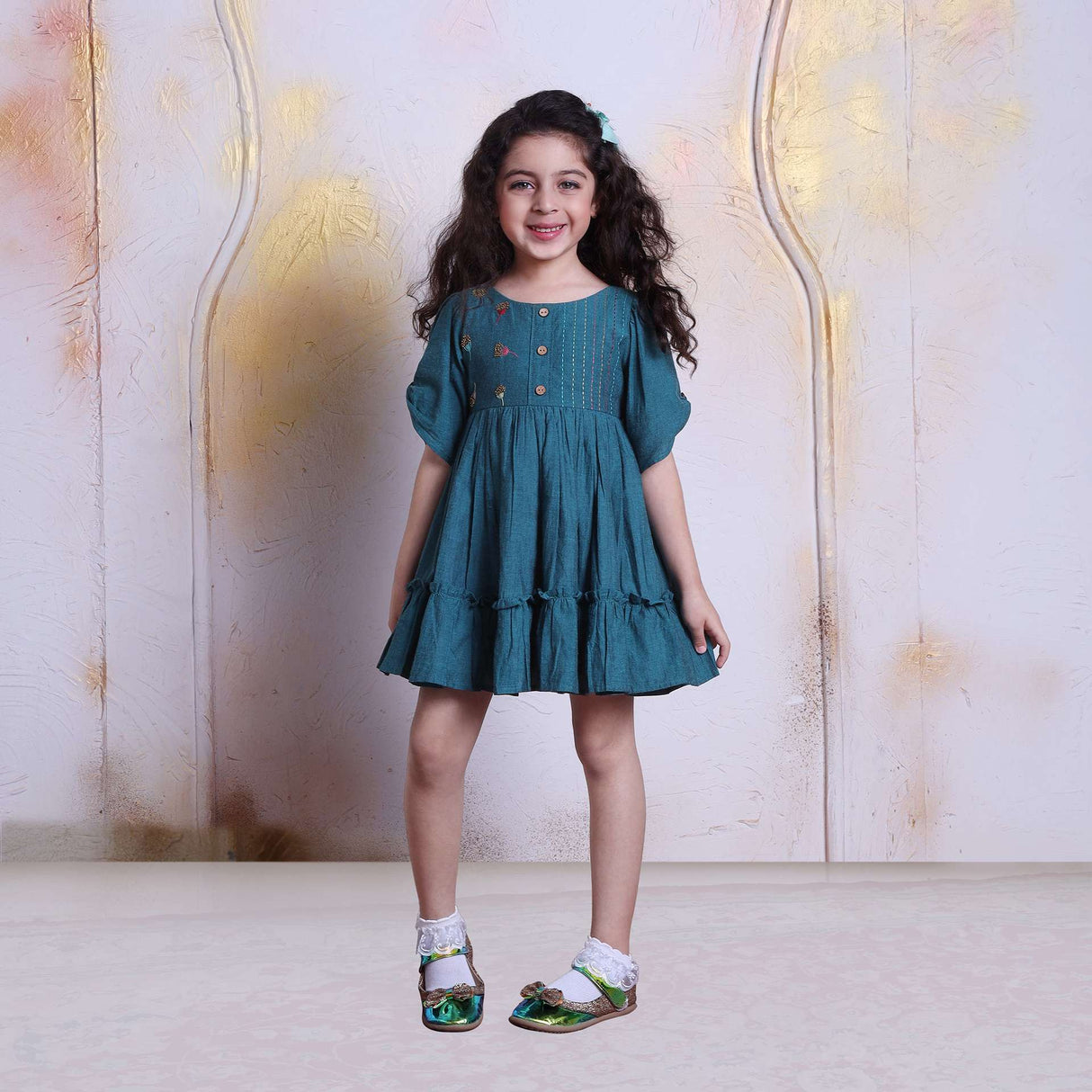 A young girl in peacock blue cotton dress with beautiful bead work, hand embroidery and wooden buttons