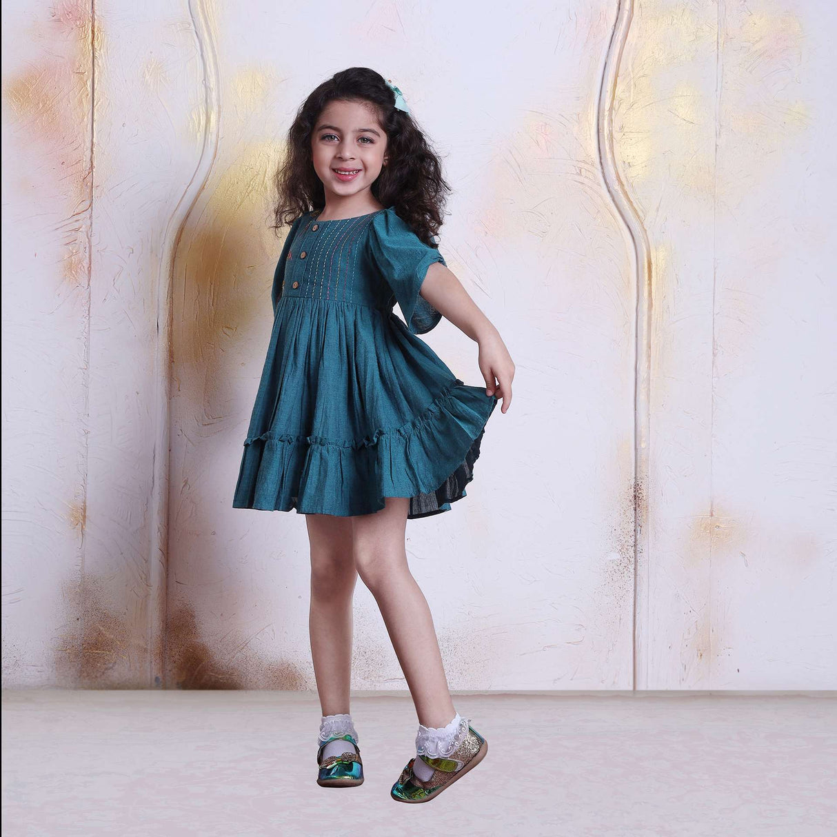 Smiling girl twirls in a green chambray dress with wood buttons
