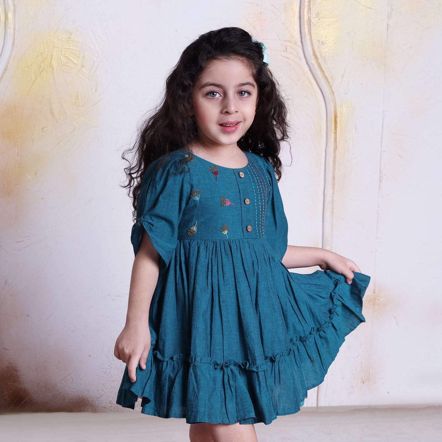 A young girl in peacock blue cotton dress with beautiful bead work, hand embroidery and wooden buttons