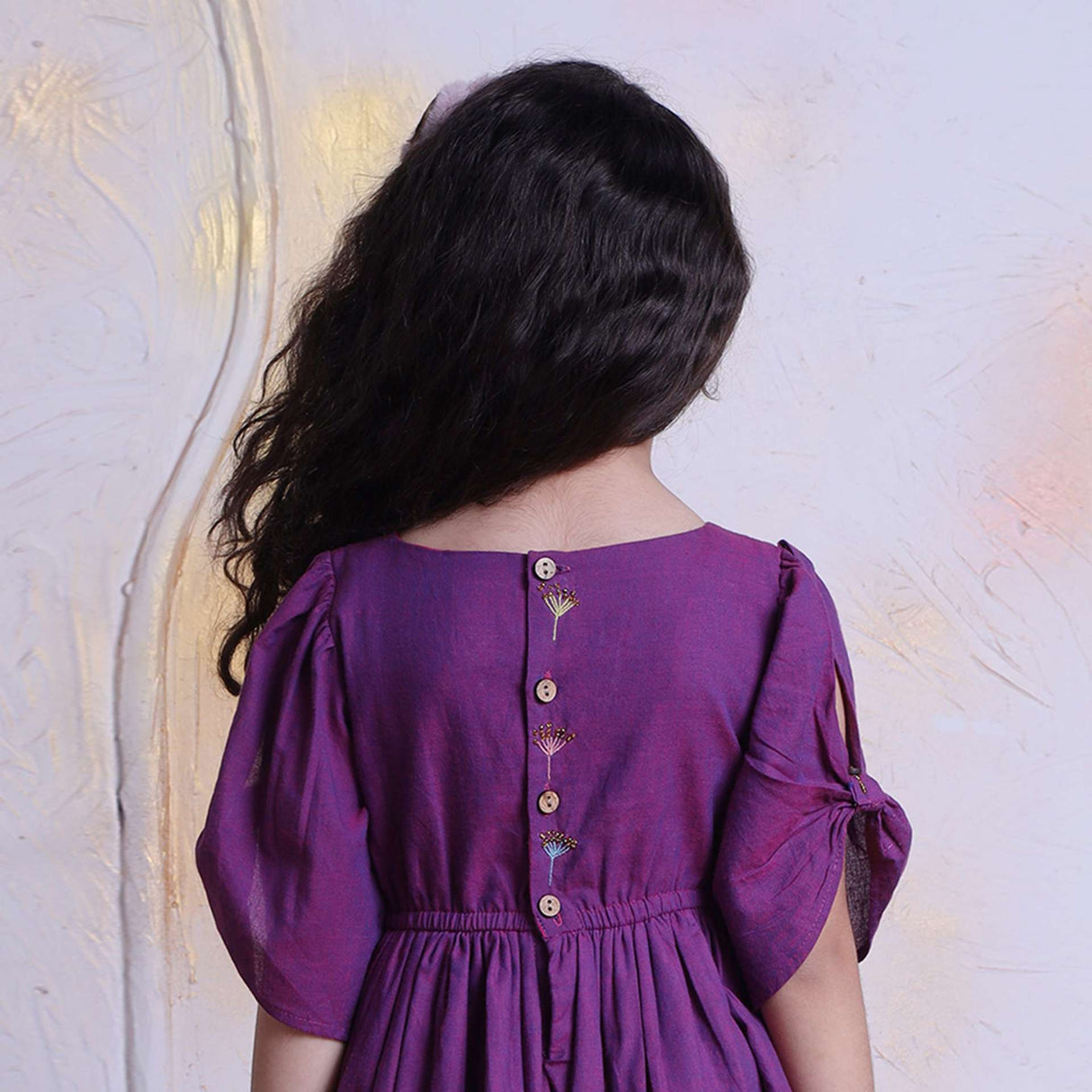 Rear close-up image of a little girl in berry pink hand embroidered cotton dress