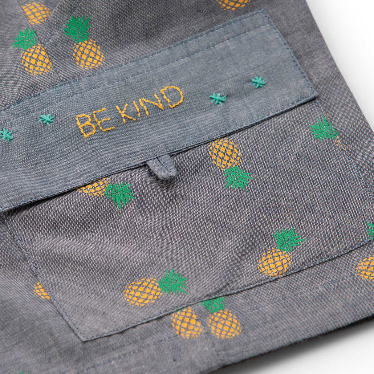 Flatlay of pineapple printed grey cotton shorts with hand embroidered message on pocket flap and elastic waist