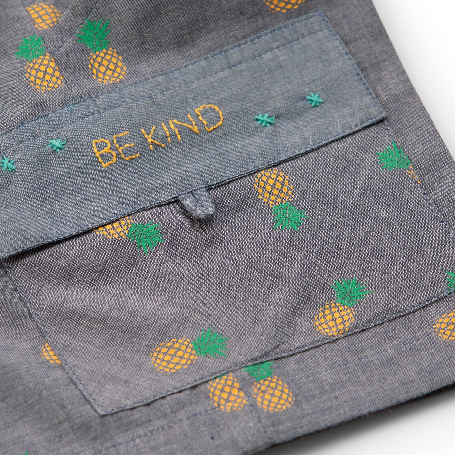 Flatlay of pineapple printed grey cotton shorts with hand embroidered message on pocket flap and elastic waist