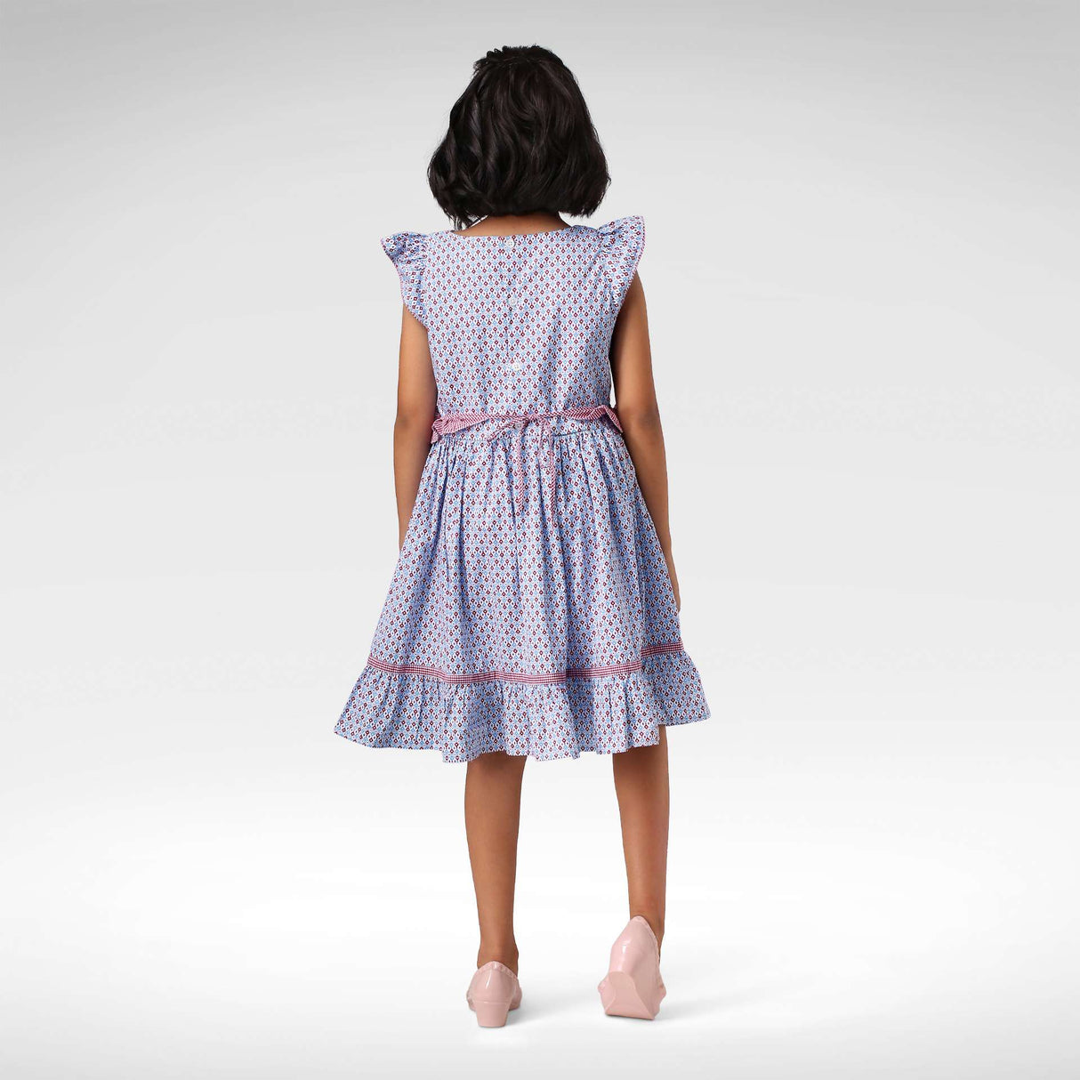 Back view of girl wearing a ruffle hem , flutter sleeve printed dress with a back waist tie