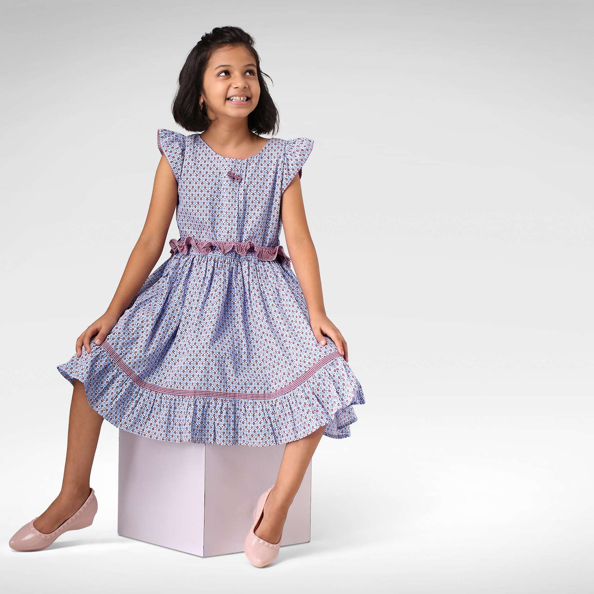 Girl seated with ruffle belt and flutter sleeve dress in red and blue print