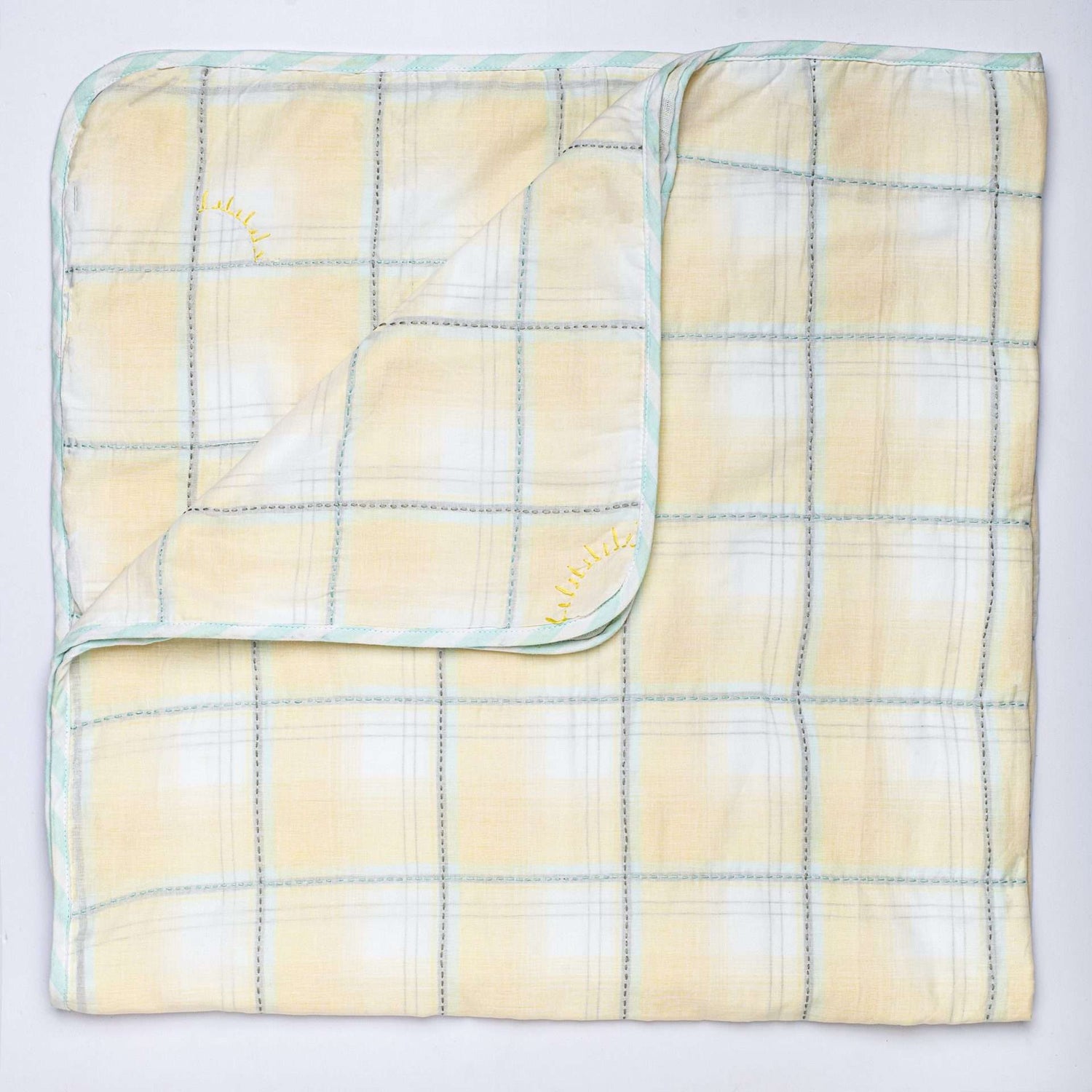 Flatlay of yellow checked blanket with hand embroidered kantha stitching between squares