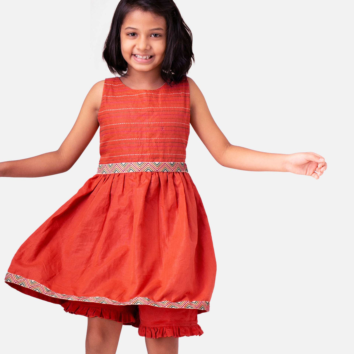A girl in chic burnt-orange linen dress with colourful embroidered waistline with a Kantha-work hand-embroidered bodice