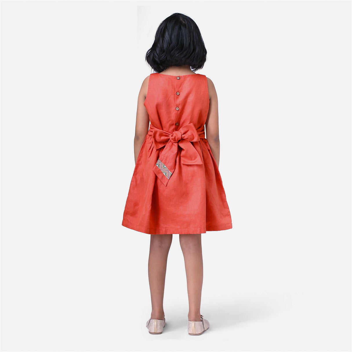 A girl in chic burnt-orange linen dress with colourful embroidered waistline with a Kantha-work hand-embroidered bodice