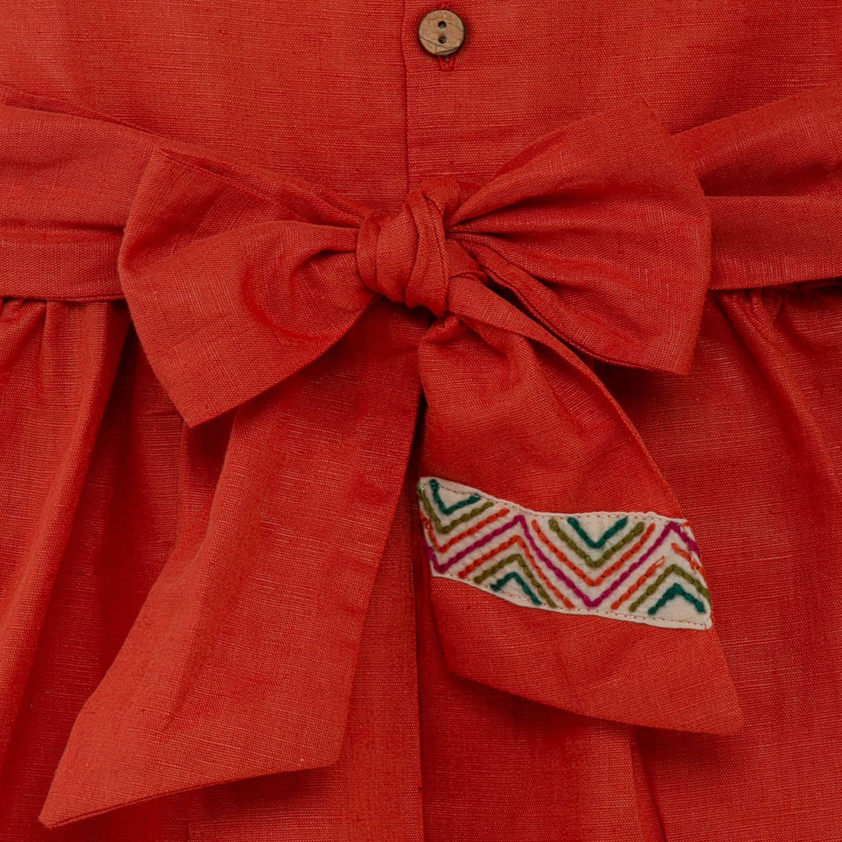 Close-up of the back bow of burnt-orange linen dress with colourful Kantha-work hand-embroidered details
