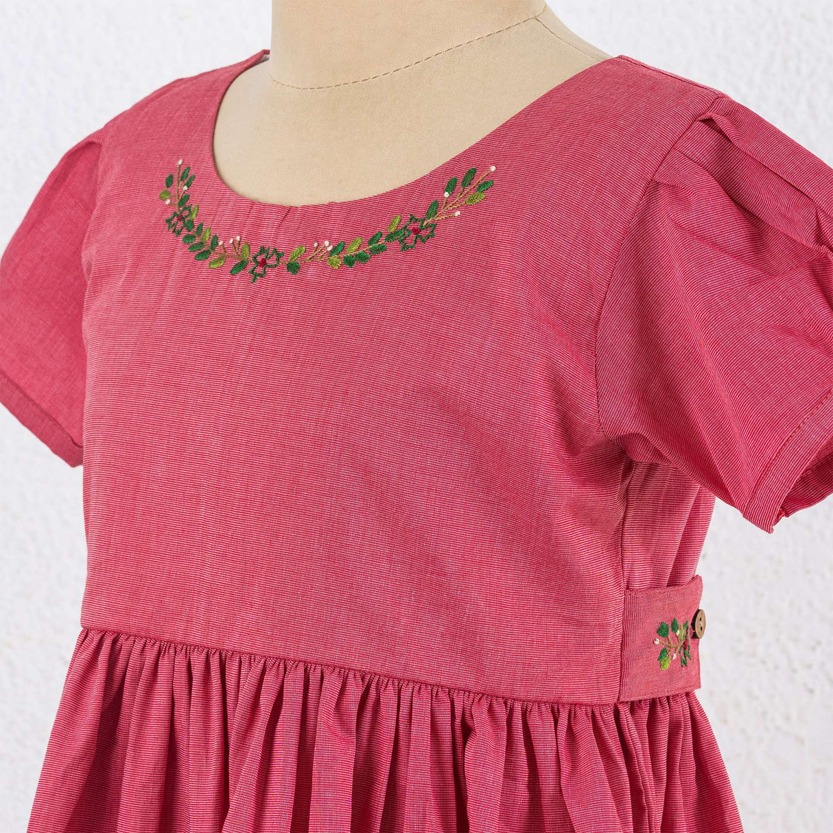 Close up of red chambray dress with hand embroidered neckline, puff sleeves, and pleated hem