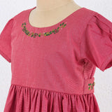 Close up of red chambray dress with hand embroidered neckline, puff sleeves, and pleated hem