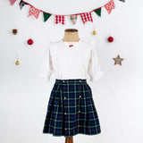 Mannequin shot of navy tartan wrap skirt paired with a frilly white cotton blouse with a little red satin bow