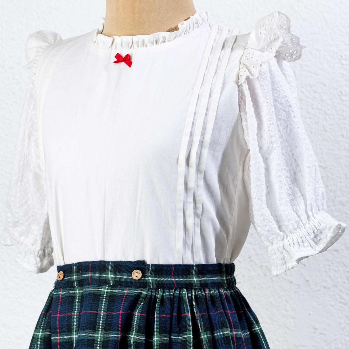 Close-up of tartan wrap skirt in navy blue with wood buttons paired with white bouse with pintucks