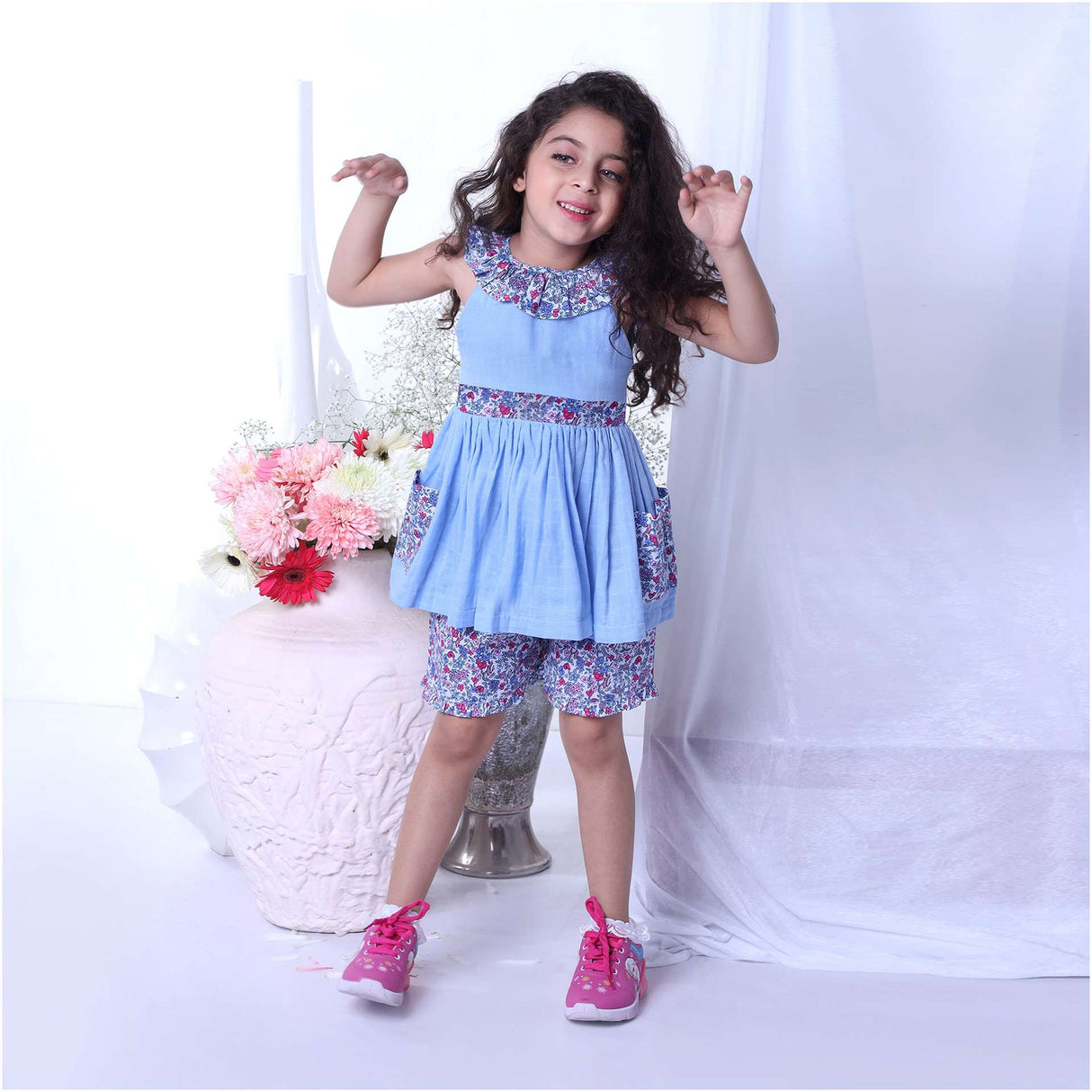 A girl in blue double gauze cotton tunic with floral ruffled neckline and tie-up belt paired with matching floral shorts