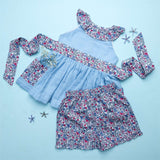 Flatlay of blue double gauze cotton tunic with floral ruffles and tie-up belt paired with matching floral shorts