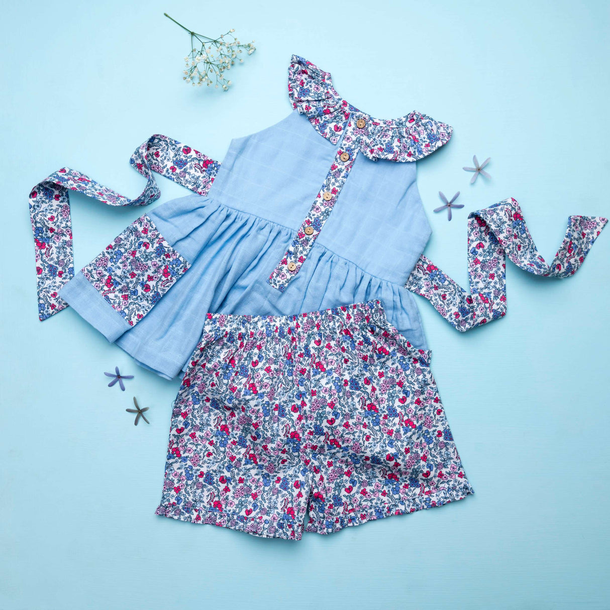 Flatlay of blue double gauze cotton tunic with floral ruffles and tie-up belt paired with matching floral shorts