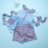 Flatlay of blue double gauze cotton tunic with floral ruffles and tie-up belt paired with matching floral shorts