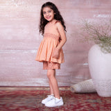 A little girl in peach gauze tunic with ruffles, hand embroidery and ties in a floral trim, with matching floral shorts