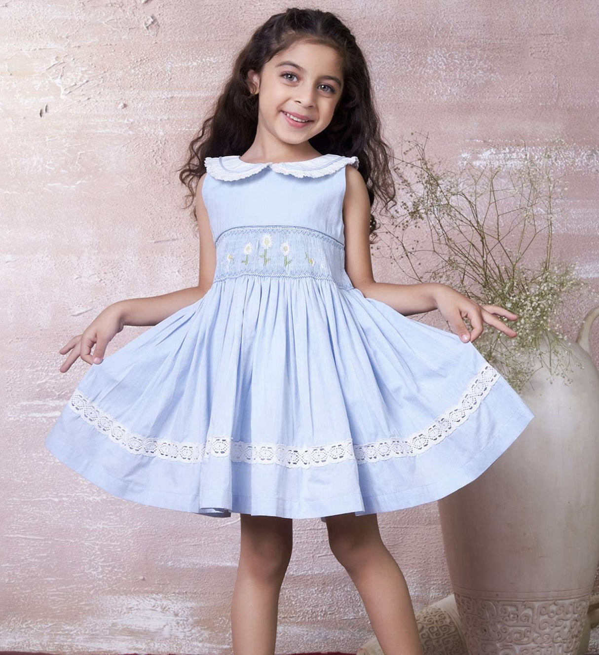 A little girl in blue hand-smocked dress with a lace insert on the skirt and a detailed collar with lace and cord piping