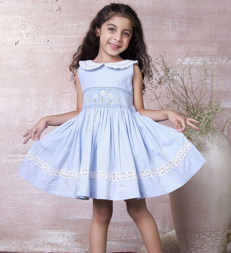 A little girl in blue hand-smocked dress with a lace insert on the skirt and a detailed collar with lace and cord piping