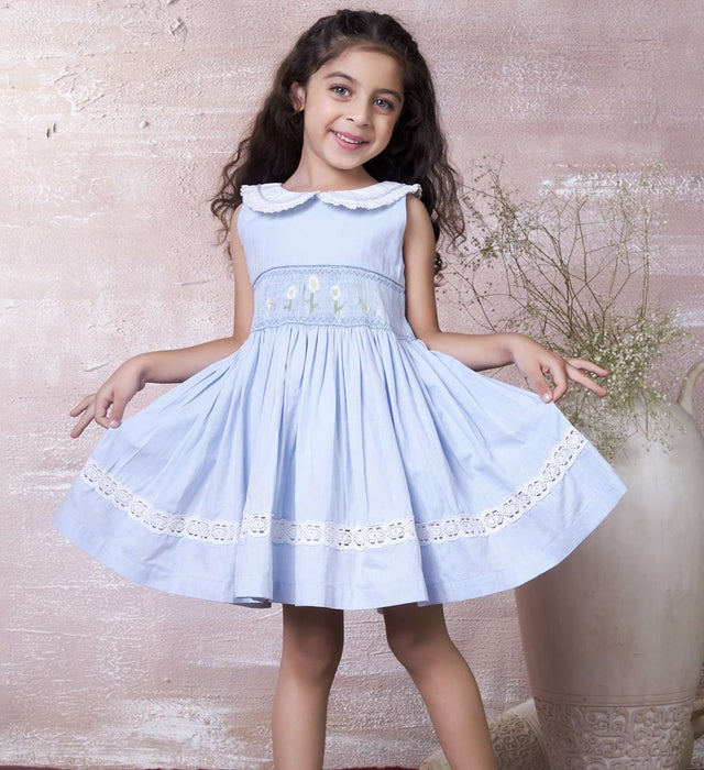 A little girl in blue hand-smocked dress with a lace insert on the skirt and a detailed collar with lace and cord piping
