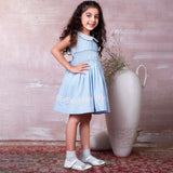 A little girl in blue hand-smocked dress with a lace insert on the skirt and a detailed collar with lace and cord piping