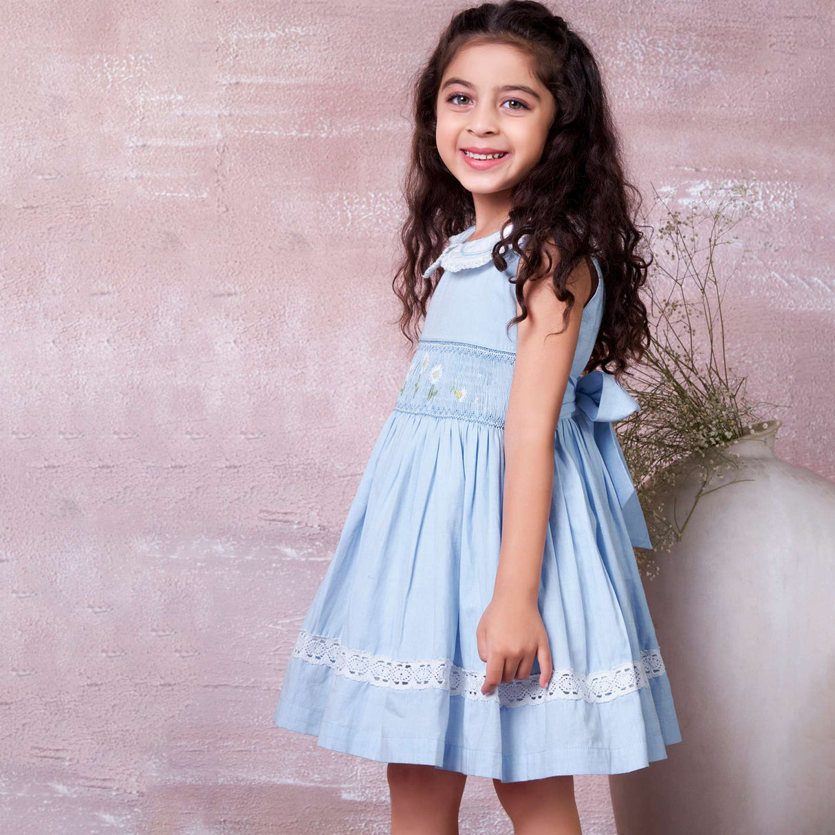 A little girl in blue hand-smocked dress with a lace insert on the skirt and a detailed collar with lace and cord piping