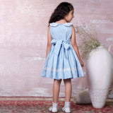 A little girl in blue hand-smocked dress with a lace insert on the skirt and a detailed collar with lace and cord piping