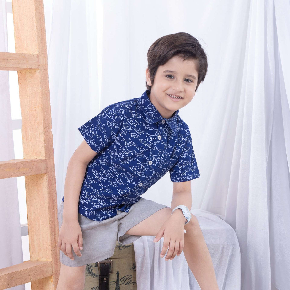 Boy wears a shark print half sleeve shirt and smiles at the camera