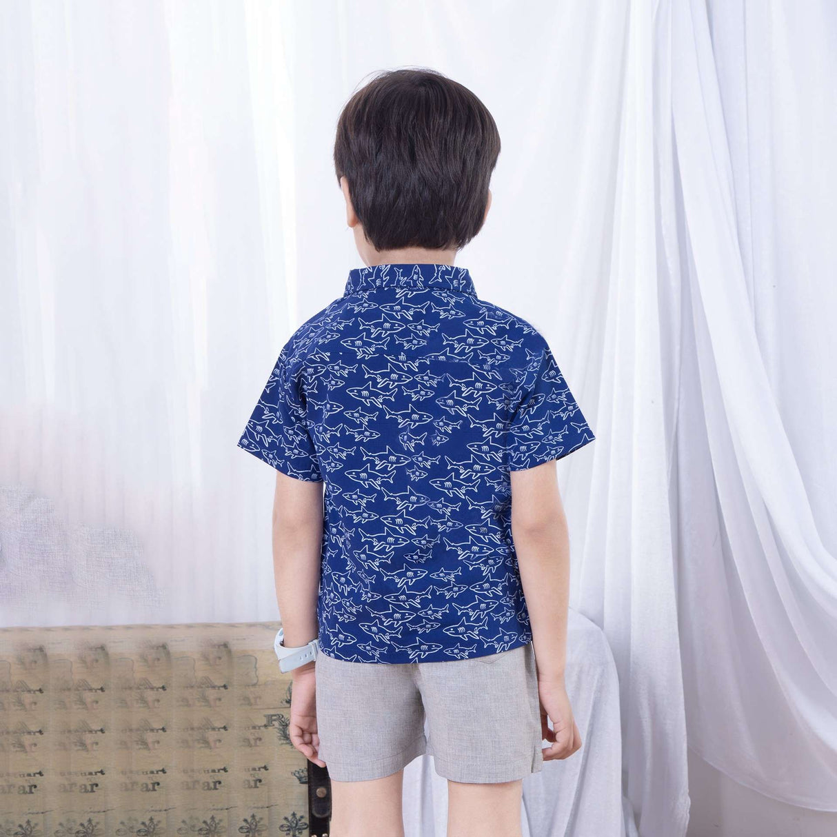 Back view of bot wearing a shark print half sleeve navy blue casual shirt and khaki cargo pocket shorts