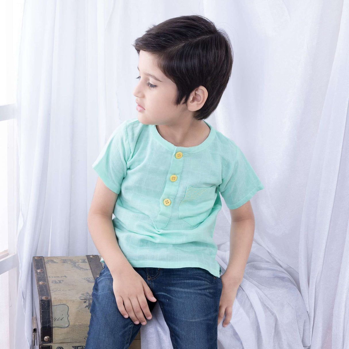 Boy seated wearing jeans and a aqua green polo half sleeve gauze shirt