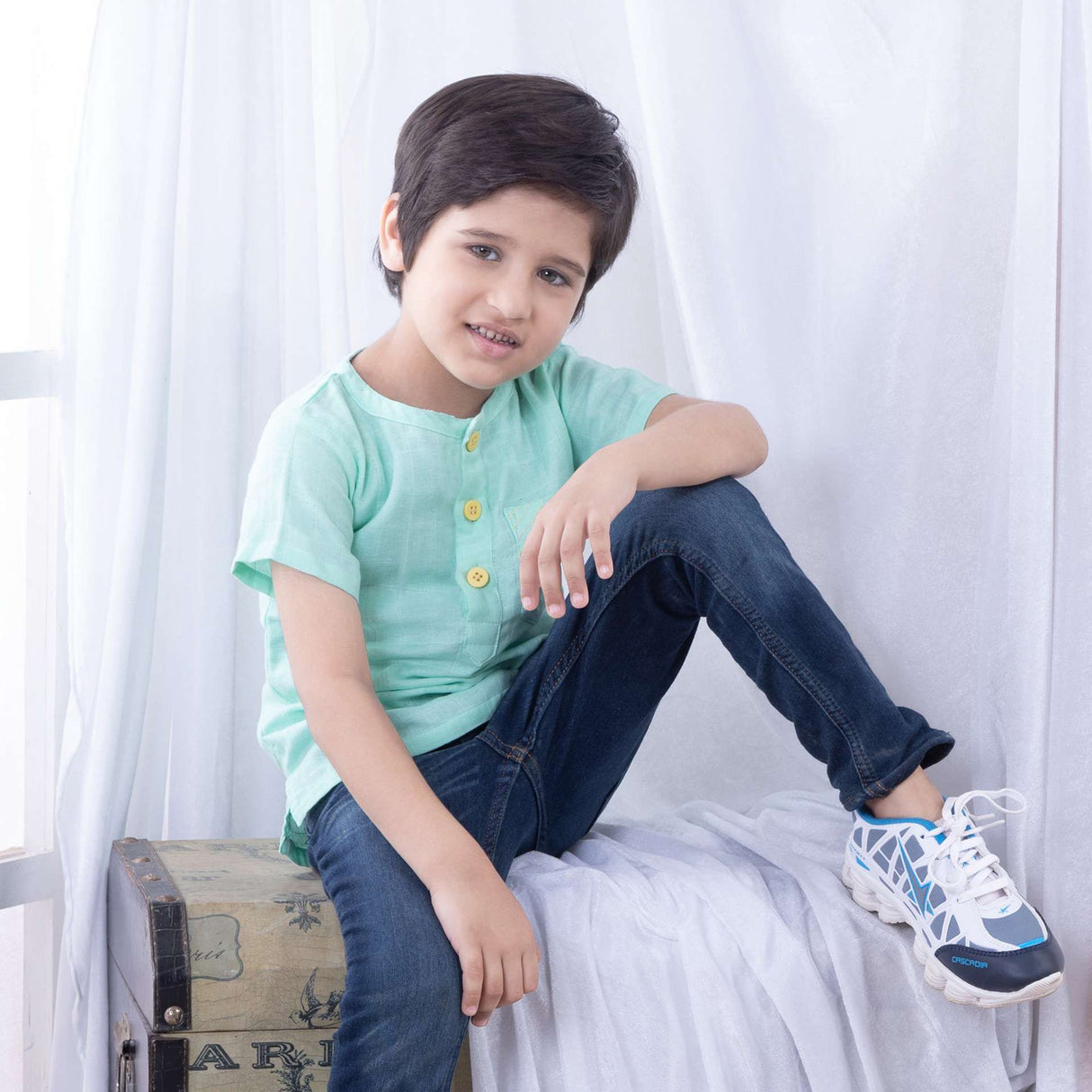 A little boy in aqua gauze boy's shirt with hand embroidered front pocket and yellow buttons