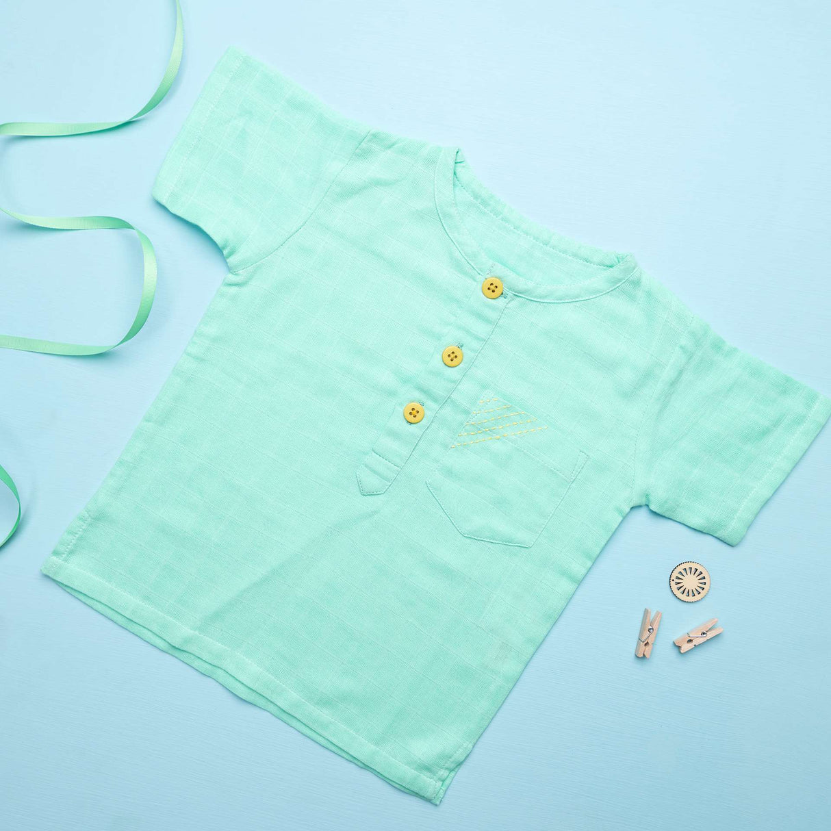 Flatlay of aqua gauze boy's shirt with hand embroidered front pocket and yellow buttons