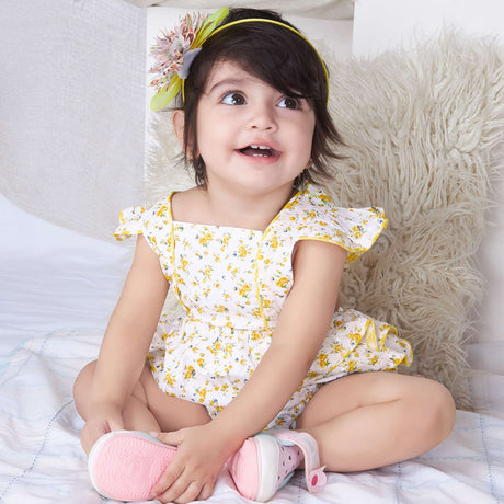A baby girl in yellow floral printed onesie with back crossover straps and ruffles on the bottom with contrast trims