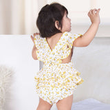 A baby girl in yellow floral printed onesie with back crossover straps and ruffles on the bottom with contrast trims
