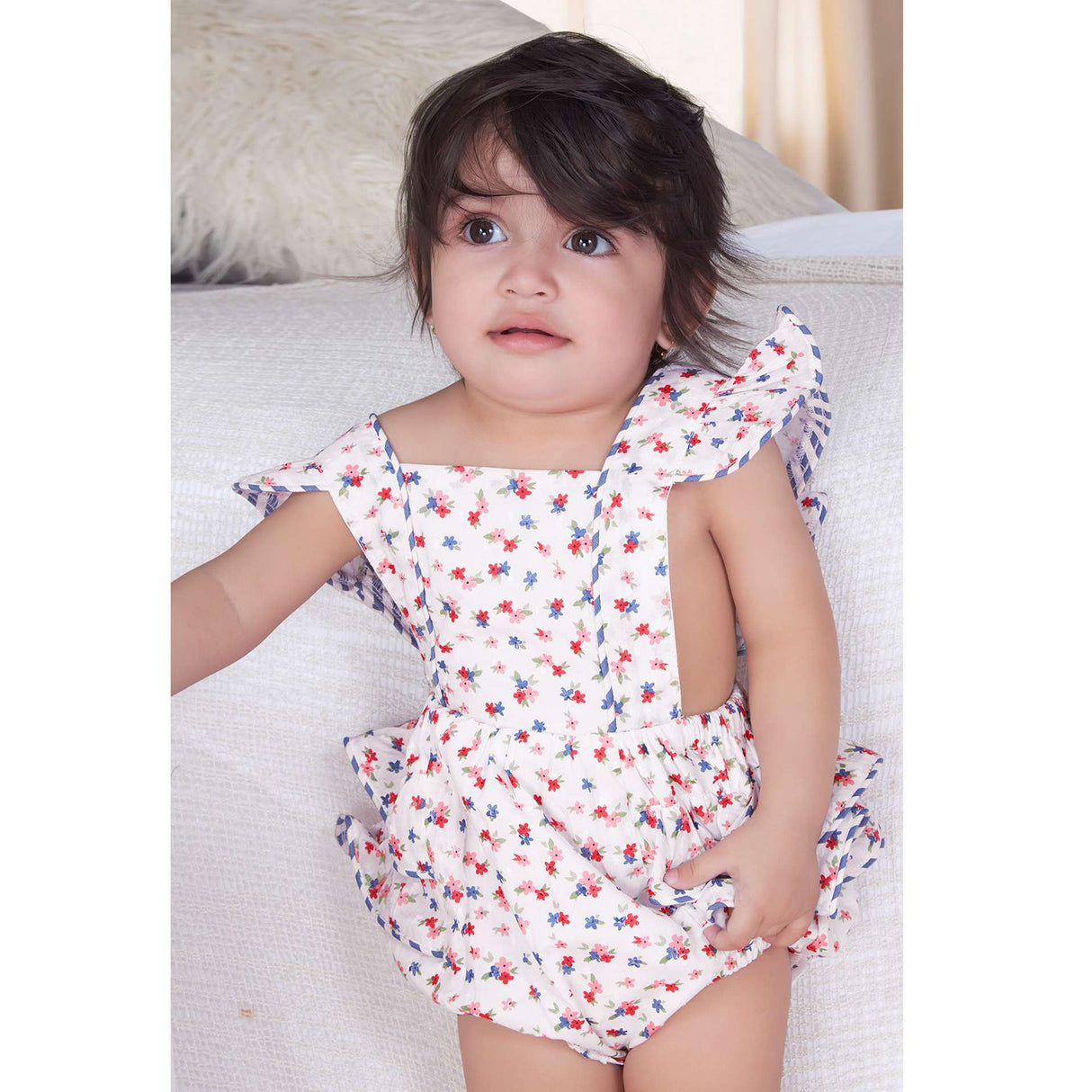 A baby girl in blue floral printed onesie with back crossover straps and ruffles on the bottom with contrast trims