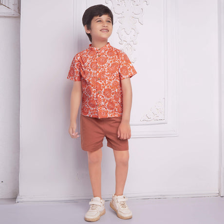 Smiling boy wearing an orange floral printed mandarin collared shirt matched with rust short
